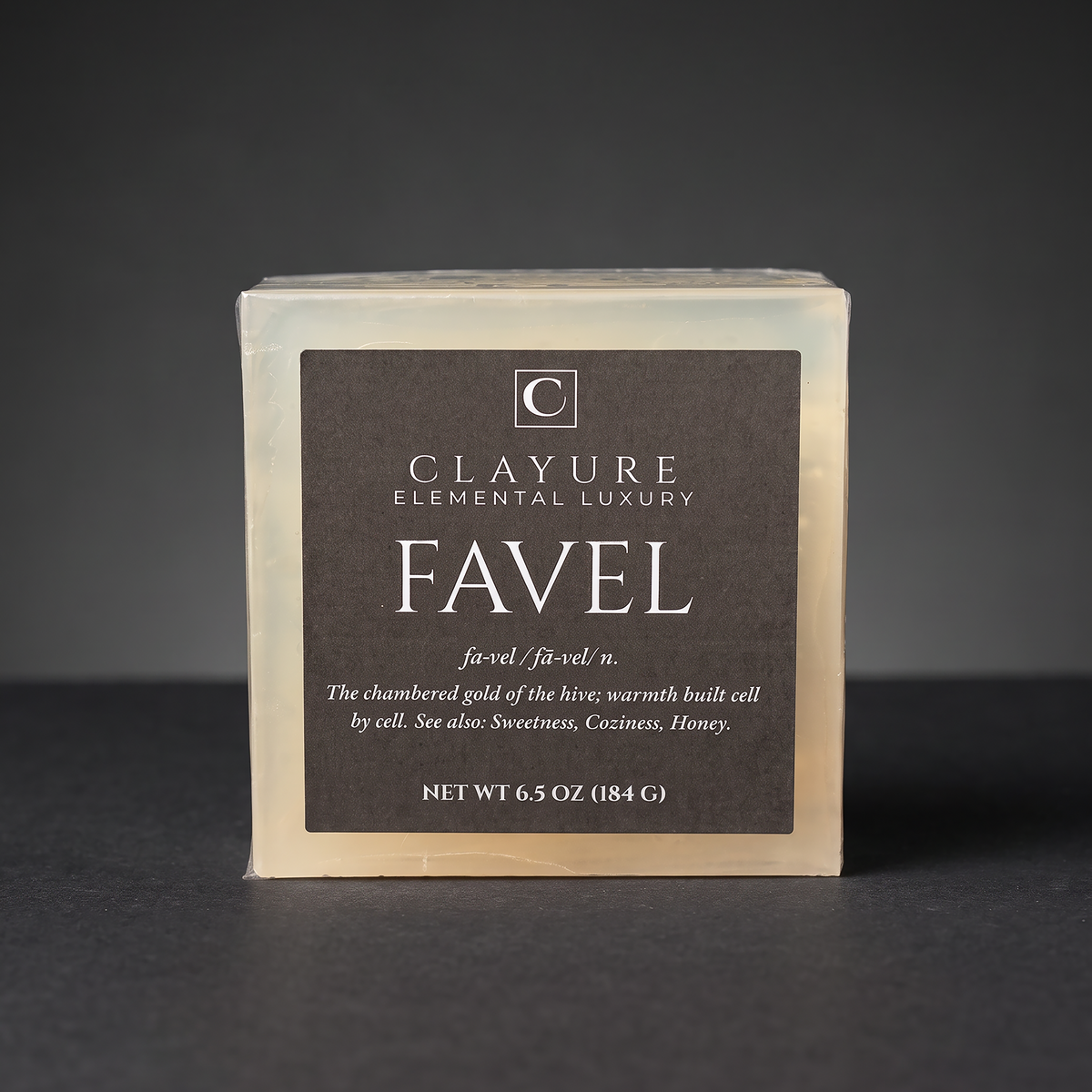 A square bar soap labeled 'Clayure Elemental Luxury Favel' on a dark gray background. The soap is Translucent-colored with a large dark black front label and white text.