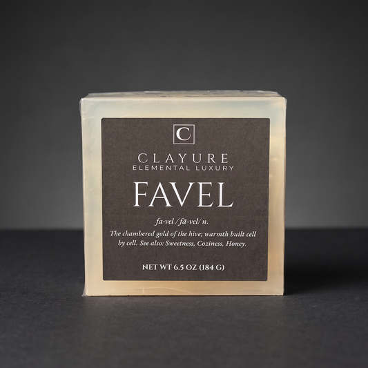 A square bar soap labeled 'Clayure Elemental Luxury Favel' on a dark gray background. The soap is Translucent-colored with a large dark black front label and white text.