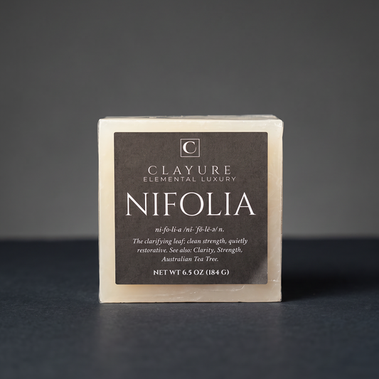 A single square bar of Clayure Nifolia soap standing upright on a dark surface against a dark gray background. The soap has a Translucent-colored outer edge and a large dark black label with white text.
